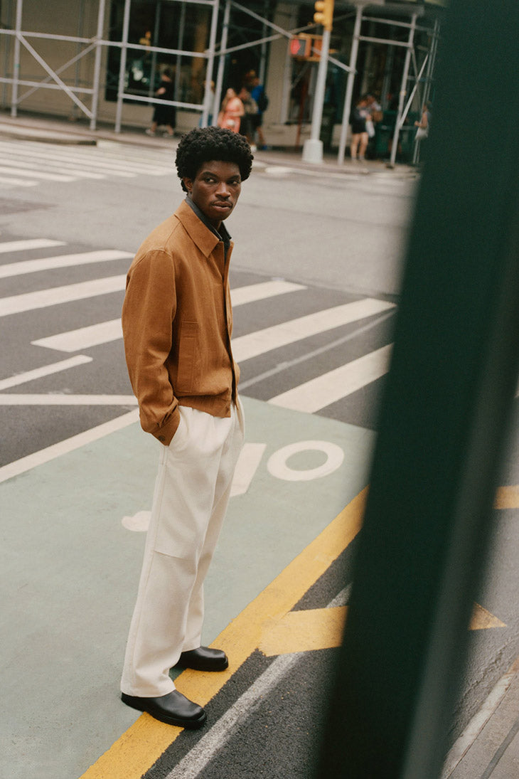 Man wearing an orange jacket and white trousers, standing in the street