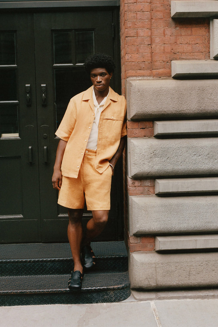 Man wearing an orange jacket and shorts, standing in a doorway